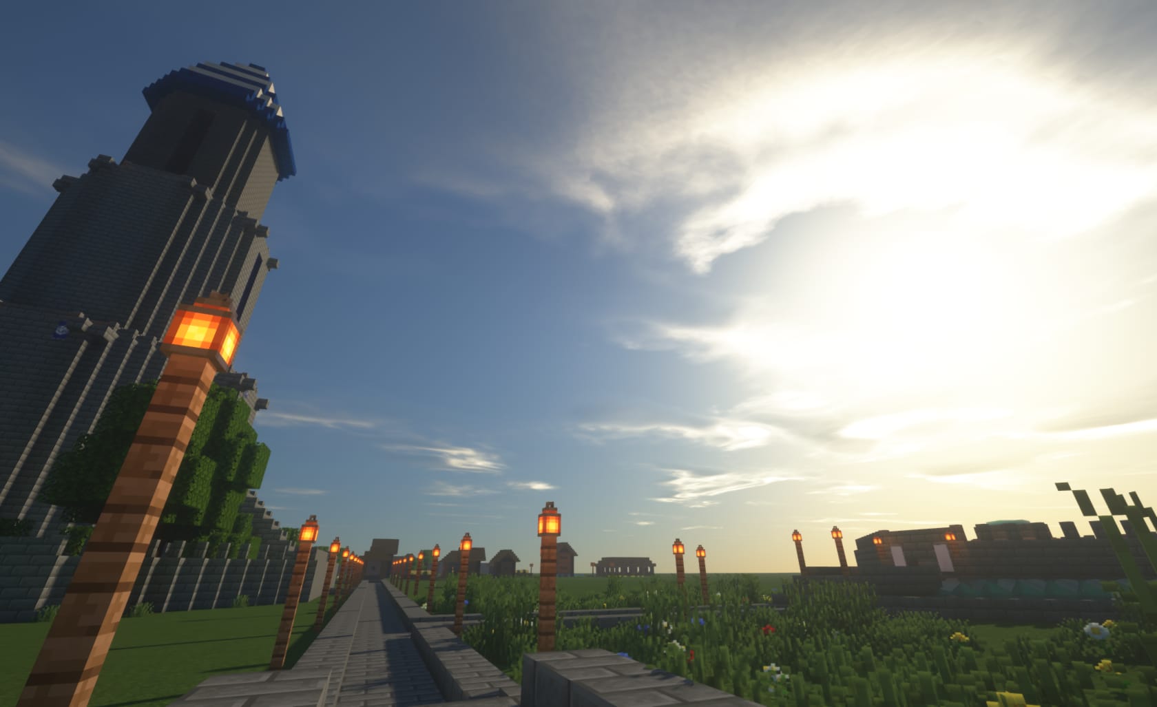 Screenshot of Minecraft game depicting: Grassy landscape with a tower on the left with a blue and white top, a stone path down the center and a building on the right.