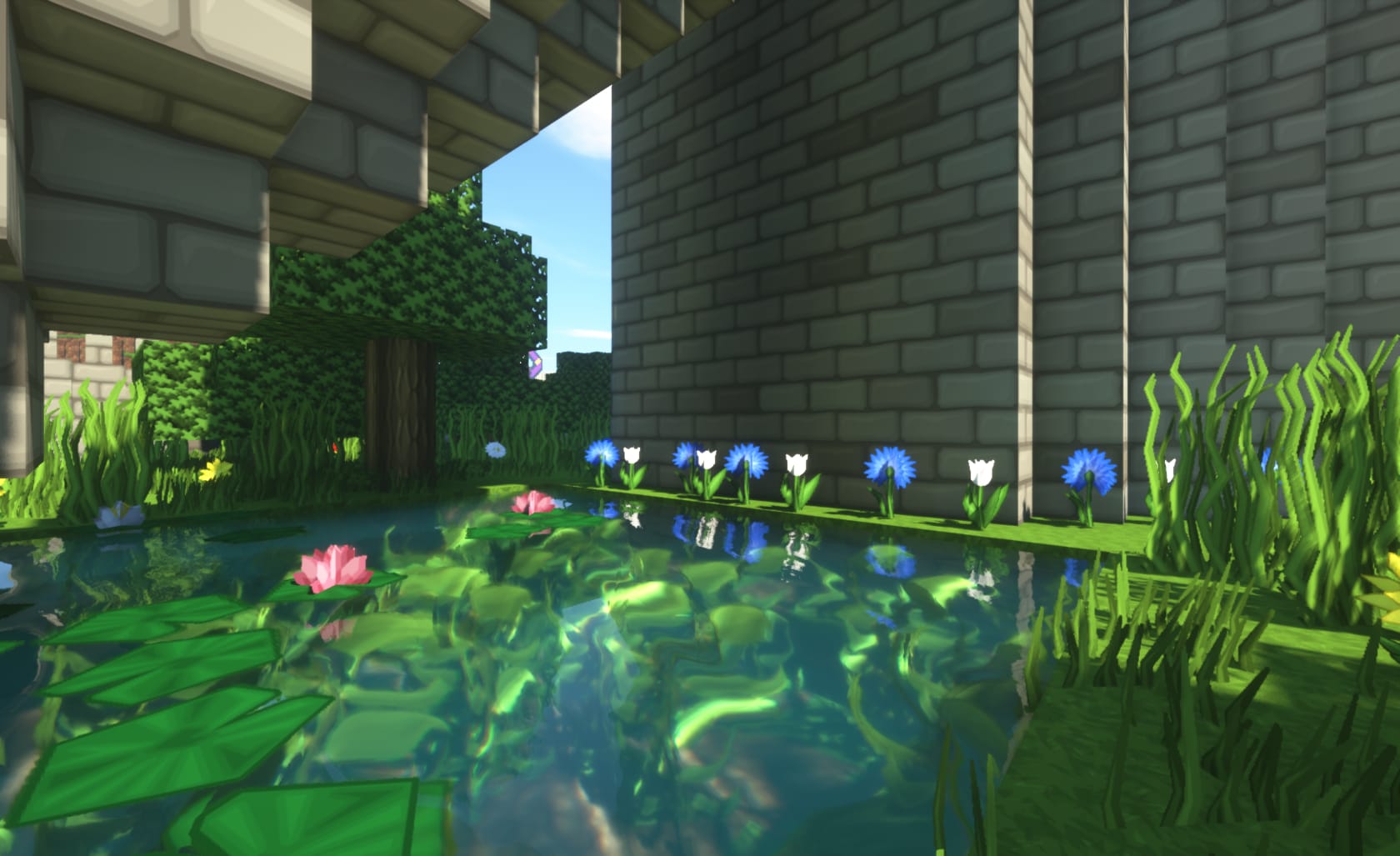 Screenshot of Minecraft game (Using PureBDCraft Minecraft Resource pack https://bdcraft.net) depicting: A pool of water with lily pads surrounded by flowers with a bridge overhead with a building on the right.