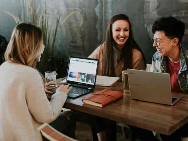 group of people around a table smiling with laptops on a table